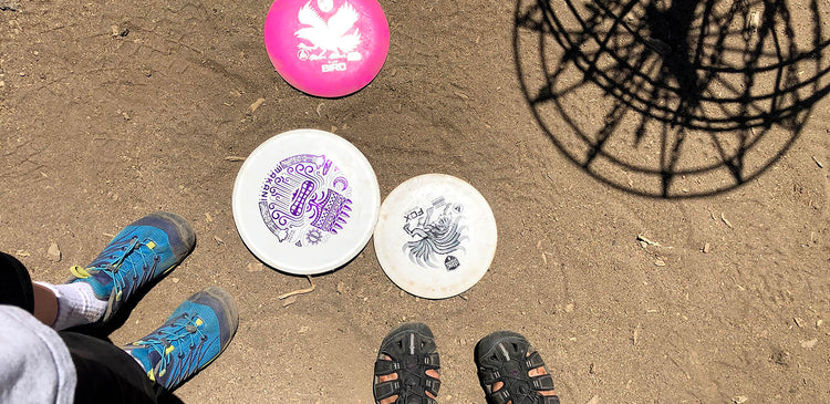 An overhead shot of KEEN shoes and discs at a disc golf basket