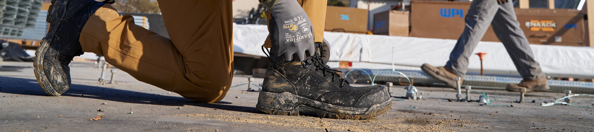 A person kneeling in a pair of black KEEN work boots, on a job site.
