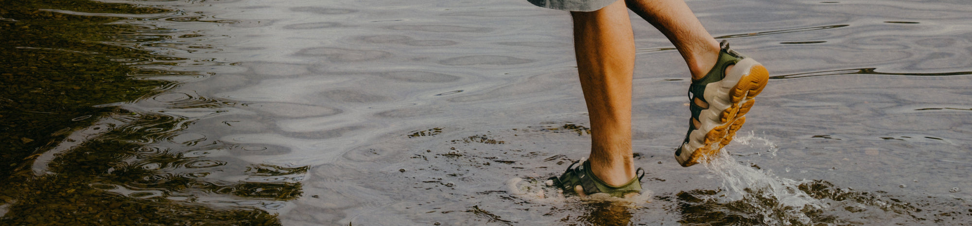 A person wearing KEEN water sandals, walking in shallow water.