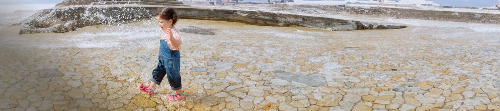 toddler kicking up water on sandstone pavers in KEEN water sandals