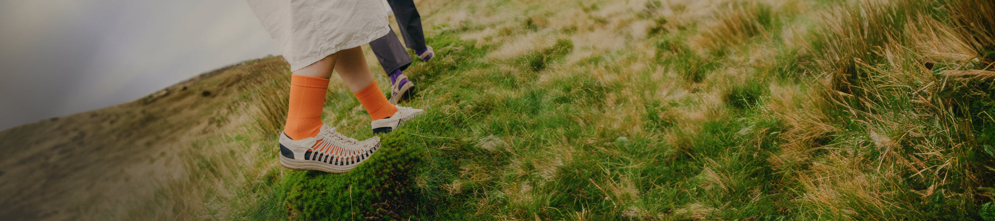 kneed down shot of two people wearing UNEEK sandals walking on moss
