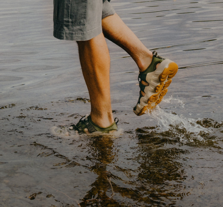 A person walking in shallow water, wearing a pair of Hyperport H2 sandals.