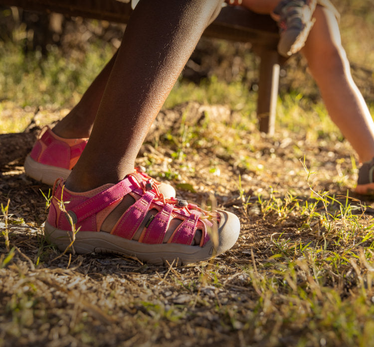 A child wearing a pair of pink and orange KEEN sandals outside.