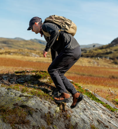 Man wearing brown Targhee IV hiking boots and hiking up rocky surface while carrying backpack 