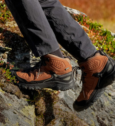 Knee-down shot of man wearing brown Targhee 3 hiking boots and walking up a steep, rocky slab. 