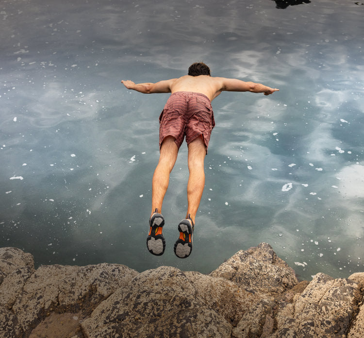 A man jumping off a large rock into a body of water.