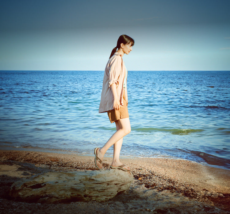 A woman walking along a beach, wearing KEEN slip-on sandals.