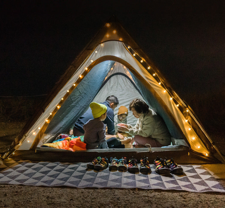 A family inside a small A-frame tent, with string lights decorating the front.