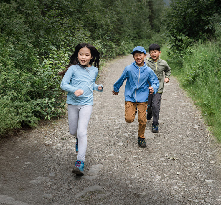 Three children running down a path outside, smiling.