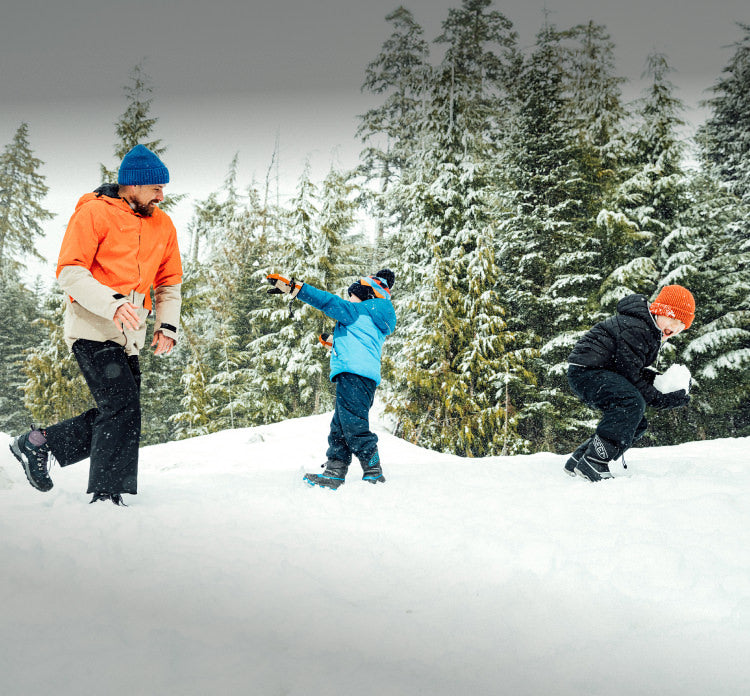An adult and two children playing together in the snow.
