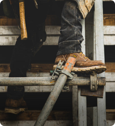 A person standing on a scaffolding, wearing a pair of brown KEEN work boots.