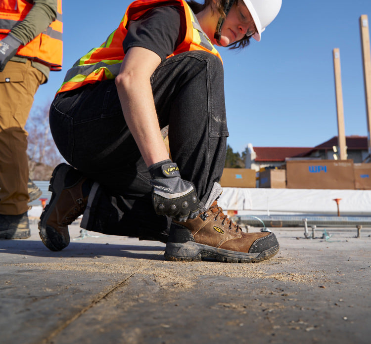 A person on a job site kneeling down, wearing a pair of brown KEEN work boots.