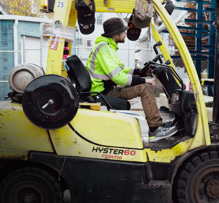 A worker operating a forklift, wearing a fluorescent yellow vest.