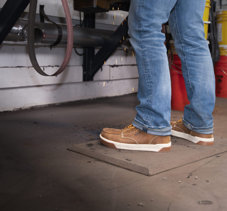 A person wearing a pair of light brown Gibson work boots.