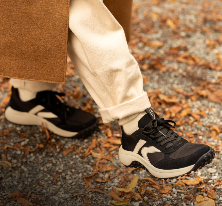 A person walking through leaves, wearing a pair of black and white KS86 sneakers.