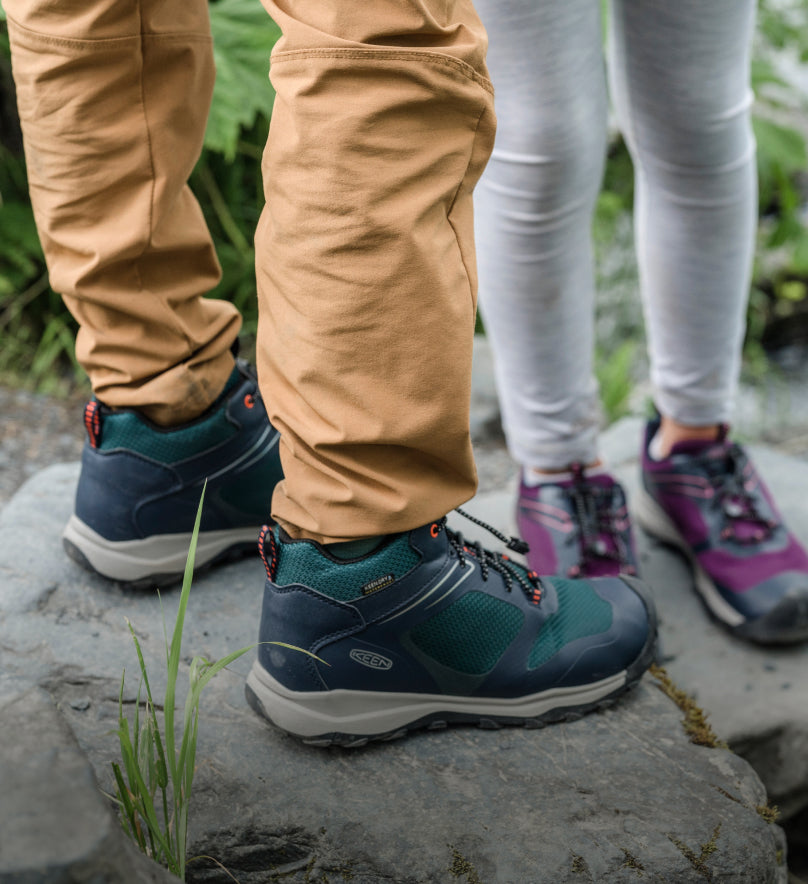 Knee-down shot of two kids wearing Wanduro waterproof shoes and standing on boulders. 