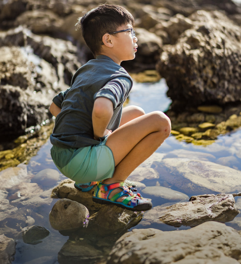 LIttle boy crouching over tidepools and wearing Tie-dye Seacamp II CNX sandals.