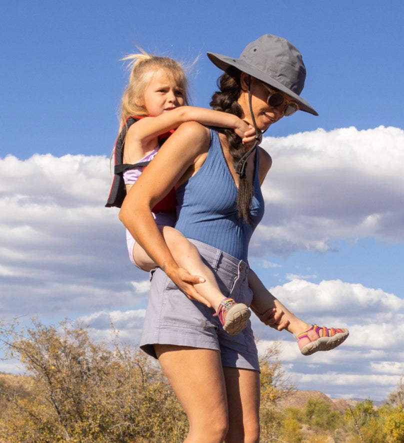 Toddler girl getting a piggy-back ride from woman in a sunhat while wearing Toddlers' Seacamp II CNX