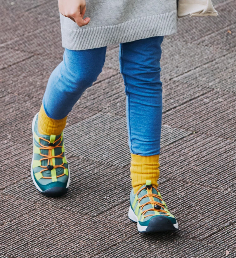 Knee-down shot of child wearing blue leggings, yellow crew socks, and green, yellow and orange Motozoa sneakers.