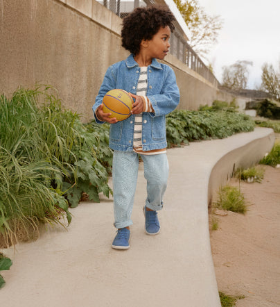 Little boy in denim jacket and jeans wearing blue KNX kids' leather sneaker while holding a basketball