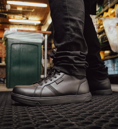 A person wearing a pair of black KEEN shoes in a kitchen.