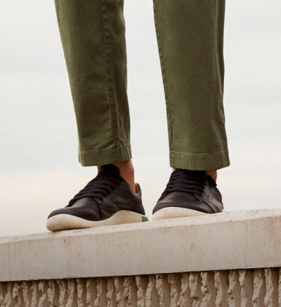 A person standing outside, wearing a pair of black and white KEEN casual sneakers.
