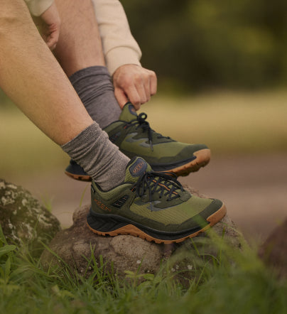 A person sitting outside, wearing a pair of green KEEN hiking shoes and socks.