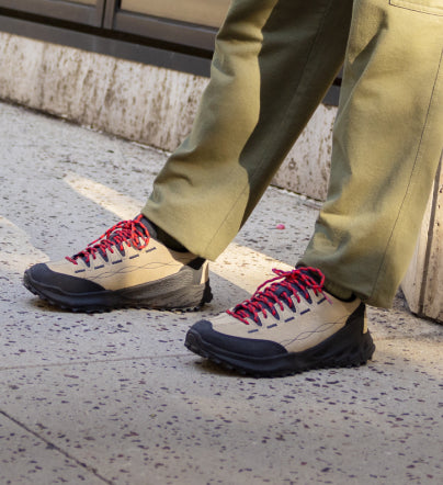 A person wearing a pair of beige and red KEEN Jasper Zionic sneakers.