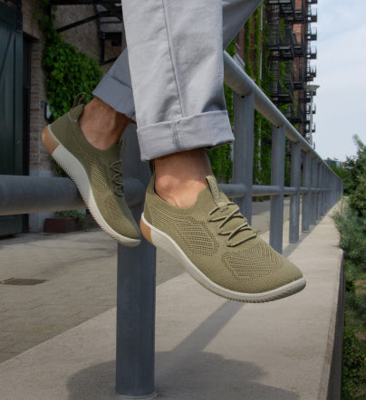 A person wearing a pair of olive green KEEN slip on sneakers.