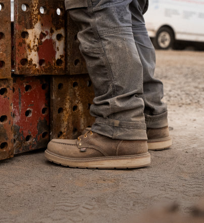 A person wearing a pair of brown KEEN work boots.