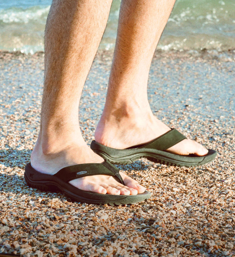 A person wearing a pair of KEEN flip flops at the beach.