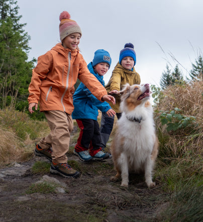 3 young boys dressed in winter gear petting a small dog on a dirt trail while wearing Targhee IV waterproof hiking boots