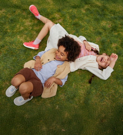 A young boy and girl laying in the grass while wearing KNX Knit Sneakers