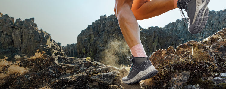 Man wearing gray NXIS boots running across rocky terrain