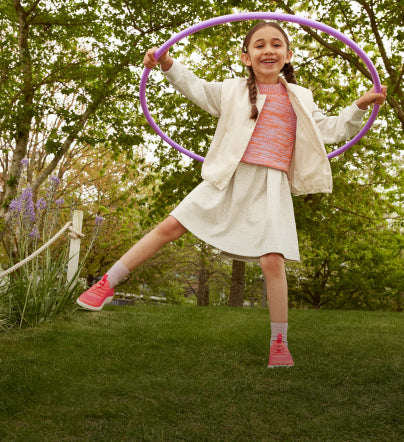 A young girl smiling, playing with a hula hoop outside.