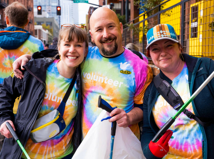 Three Keen employees wearing tie-dye volunteer shirts with garbage-collecting supplies