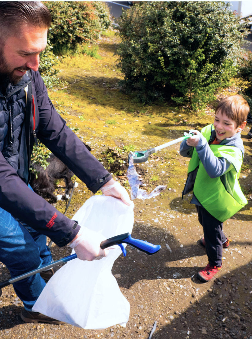 Man holding trash bag open for young child to put trash into outside