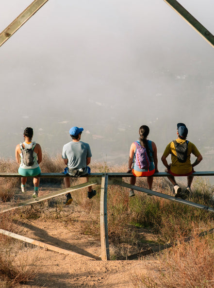4 young adults sitting on metal fence overlooking a cloudy valley