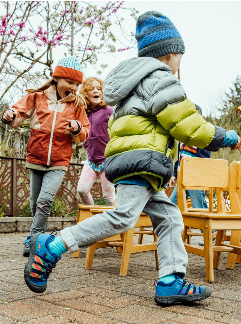 Kids wearing puffy coats and beanies on a school playground playing musical chairs
