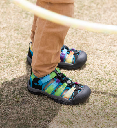 Knee-down shot of boy wearing tie-dye newport h2 sandals and standing on pavement.
