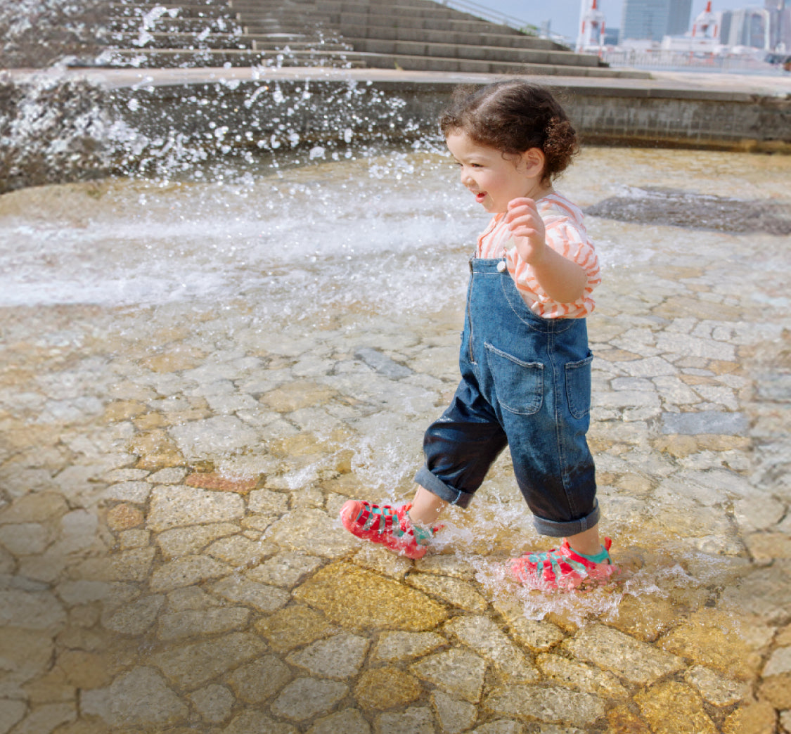 toddler kicking up water on sandstone pavers in KEEN water sandals