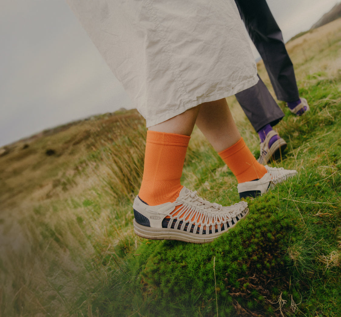 kneed down shot of two people wearing UNEEK sandals walking on moss