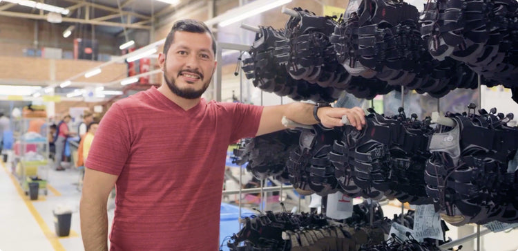 Man in red shirt standing in front of of half-made sandals in a factory