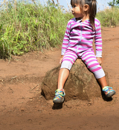Little girl wearing tie-dye newport h2 sandals and sitting on a boulder with dirt trail in the background