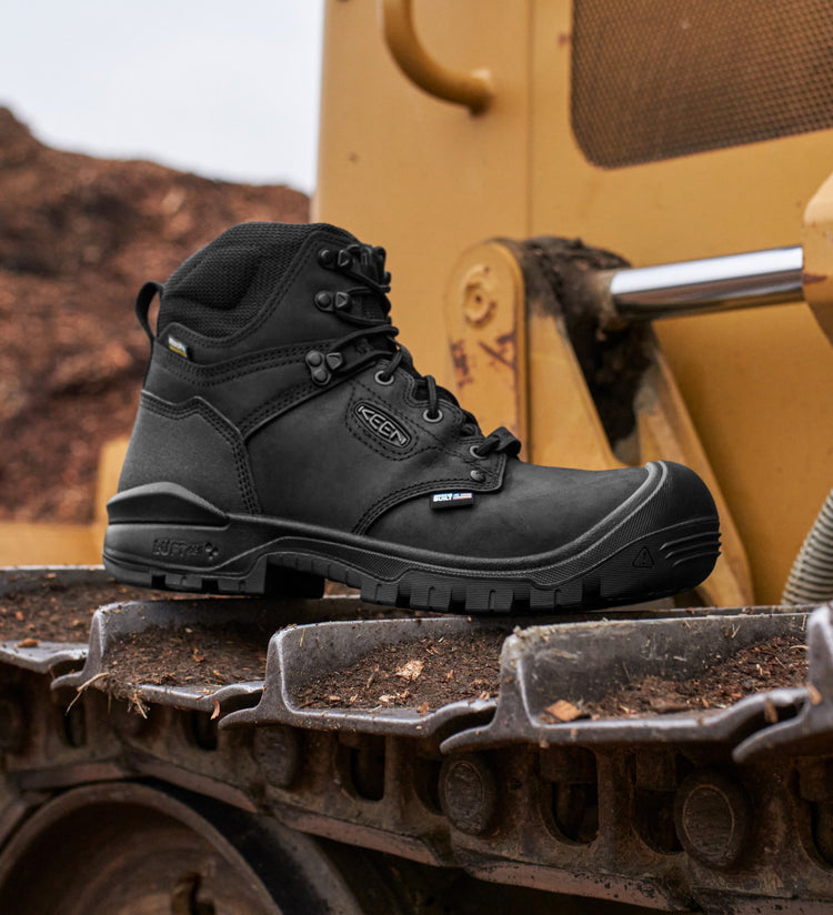 Product shot of Men's Independence work boot in front of tractor. 
