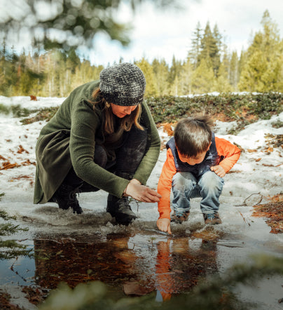Mom and child dressed for winter, crouching over snowy puddle and looking in the water while wearing Targhee IV waterproof boots.