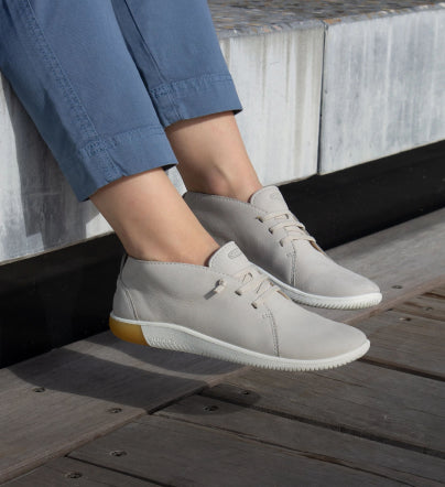 A person sitting outside, wearing a pair of grey KEEN sneakers.