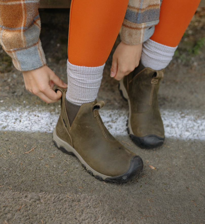 A person pulling on a pair of olive green KEEN boots.