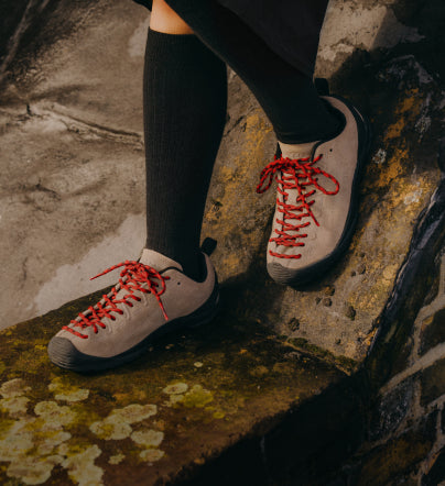 A person walking outside, wearing a pair of tan and red KEEN Jasper sneakers.