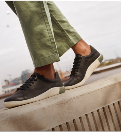 A person walking outside, wearing a pair of black and white KEEN casual sneakers.